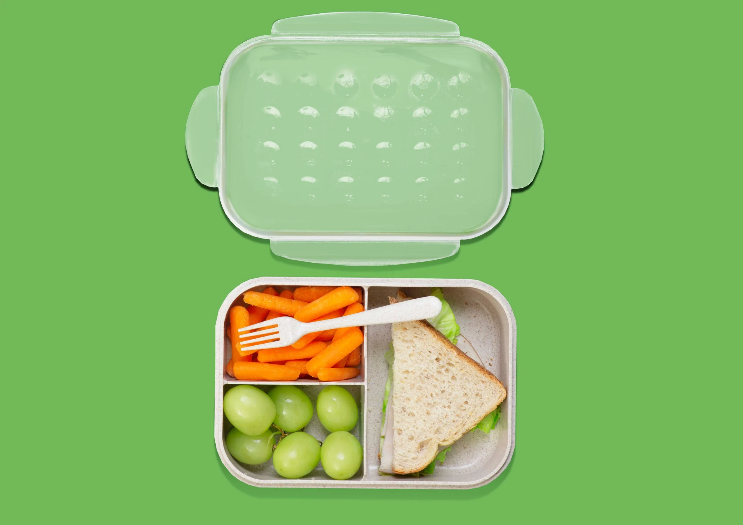Sage green bento school lunch box with sandwich, grapes and carrots beside a reusable water bottle